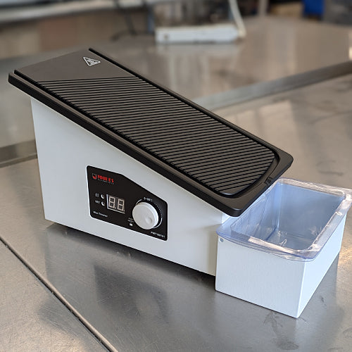 A black paraffin wax trimmer with a grooved surface and a catch basin below.