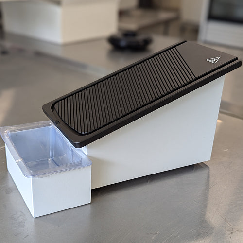 A black paraffin wax trimmer with a grooved surface and a catch basin below.