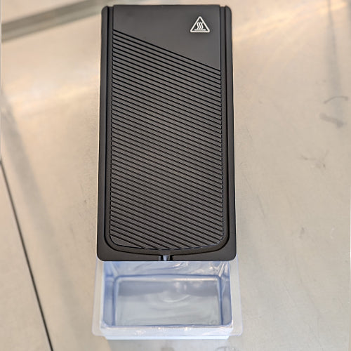 A black paraffin wax trimmer with a grooved surface and a catch basin below.