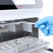 Studio product view of a gloved hand inserting a magnetic rod comb into the upper internal chamber slot of a 4E's USA 32-throughput nucleic acid extraction system against a white background, highlighting its stainless steel interior and slide-out lower platform
