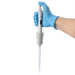 Studio product view of a 4E's USA Precipette adjustable pipette (1-10mL) being held by a hand in a blue nitrile glove against a white background, highlighting its ergonomic grip, digital display, and attached pipette tip