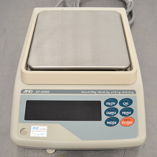 Straight-on studio view of an A&D GF-4000 precision balance on a metallic surface, featuring its square stainless steel weighing pan, light grey housing, digital display screen, and right-hand operational control buttons