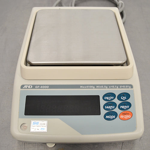 Straight-on elevated studio view of an A&D GF-4000 precision balance on a metallic surface, displaying the square stainless steel weighing pan, beige housing, digital vacuum fluorescent display, and operational keypad