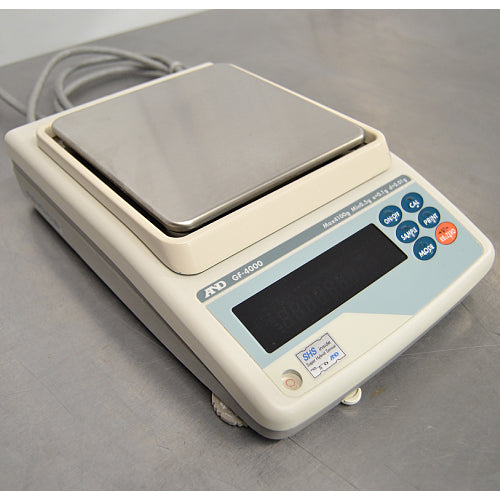 Straight-on studio view of an A&D GF-4000 precision balance on a metallic surface, featuring its square stainless steel weighing pan, light grey housing, digital display screen, and right-hand operational control buttons