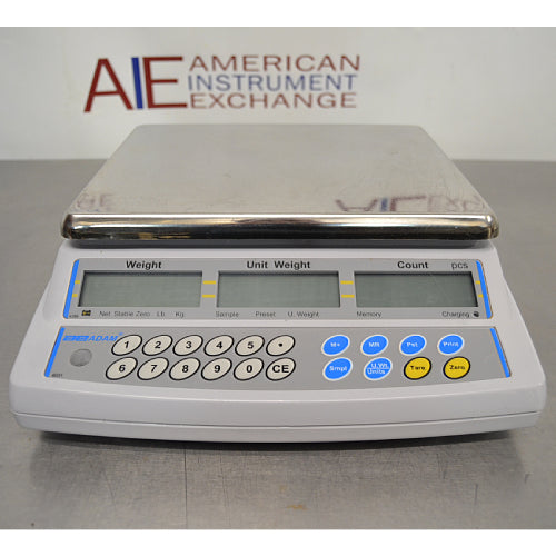 Straight-on studio view of an Adam Equipment CBC 71a digital counting scale on a metallic surface, showcasing its stainless steel weighing pan, front control panel with numeric keypad, and triple LCD displays for weight, unit weight, and count