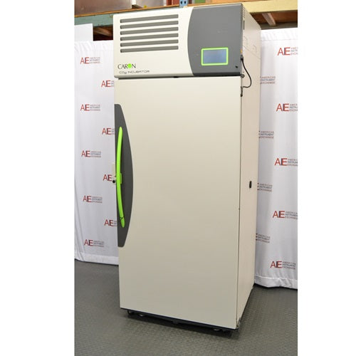 A side-angled view of the Caron 7401-33-22 reach-in CO₂ incubator, showing its light-colored exterior, top-mounted digital display, and green handle, positioned in front of an American Instrument Exchange backdrop.