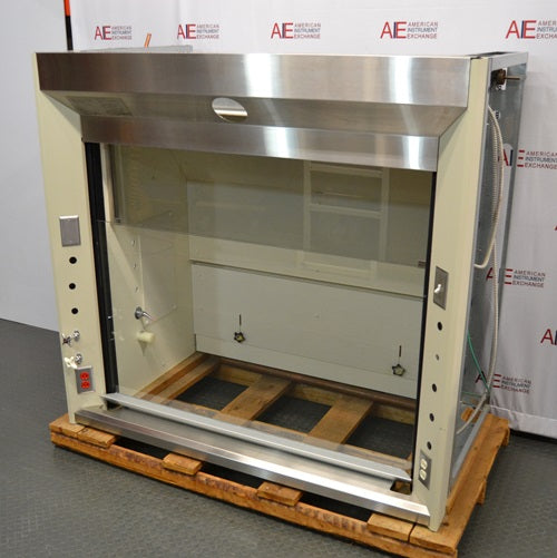 An angled view of a Jamestown chemical fume hood mounted on a wooden pallet in front of an American Instrument Exchange backdrop, displaying its stainless steel sash casing, side control panels, and interior chamber.