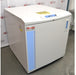 An angled view of a Thermo Scientific CryoPlus 4 cryogenic storage system resting on the floor in front of an American Instrument Exchange backdrop, showing its closed top lid, microprocessor control panel with key lock, left side casing with product label, and front face with blue vertical striping.