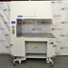 A Baker AniGARD e3 Animal Transfer Station, white in color, with a clear glass window and electronic controls on the top. It is set against a backdrop featuring the AIE Laboratory Services branding.