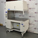 A Baker AniGARD e3 Animal Transfer Station, white in color, with a clear glass window and electronic controls on the top. It is set against a backdrop featuring the AIE Laboratory Services branding.