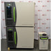 A front-facing view of a stacked Caron 6010-1 environmental chamber system, featuring two units with beige and charcoal-grey housings, bright green door handles, and an adjacent condensate recirculator, all set against an American Instrument Exchange backdrop.