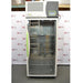 A front-facing view of a tall, upright Caron 7000-33-1 environmental chamber, featuring a full-length glass door with a signature bright green handle, a top-mounted control interface, and adjustable interior shelving against an American Instrument Exchange backdrop.