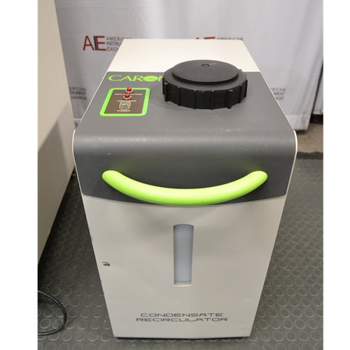 A close-up view of a Caron condensate recirculator, featuring its beige and grey exterior, bright green handle, top-mounted black cap, and a clear vertical fluid level indicator window.