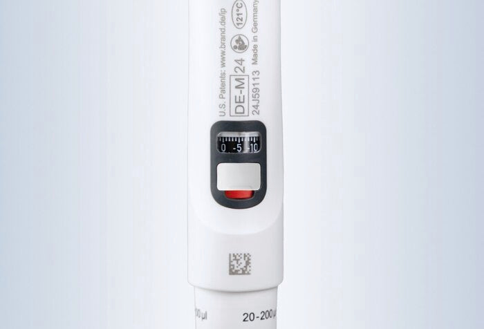 A detailed close-up view of the handle section of a white BRANDTECH Transferpette S pipette, showing the digital volume readout window, calibration adjustment slider with red accent, product markings, serial number, and 20–200 µL volume range label.