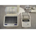 A close-up view of a Mettler Toledo SevenExcellence multiparameter meter touchscreen terminal, expansion module block, compact printer, and power supply components on a stainless steel surface.
