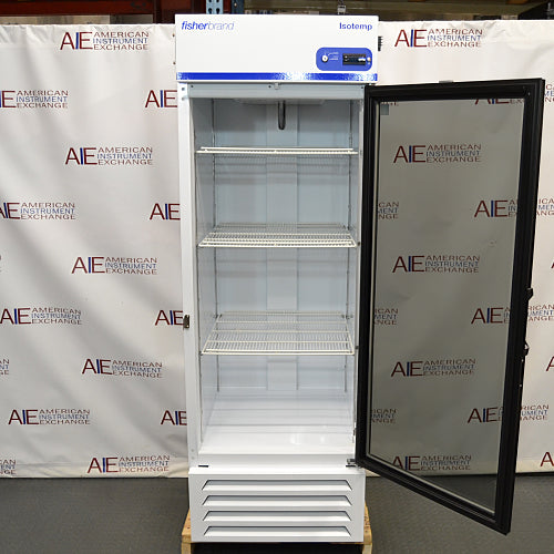 Straight-on studio view of a Fisherbrand Isotemp FBG25RPGA upright laboratory refrigerator standing on a wooden pallet against a branded backdrop, featuring a full-length black-framed glass door, top-mounted digital display console, and louvered white base