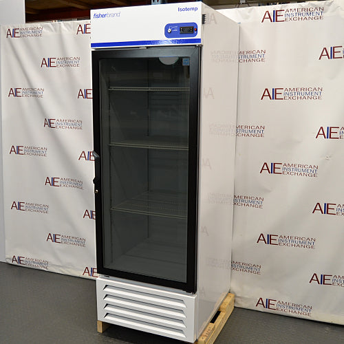 Straight-on studio view of a Fisherbrand Isotemp FBG25RPGA upright laboratory refrigerator standing on a wooden pallet against a branded backdrop, featuring a full-length black-framed glass door, top-mounted digital display console, and louvered white base