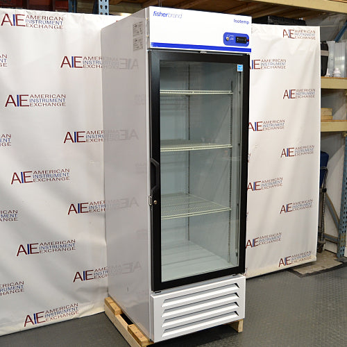 Straight-on studio view of a Fisher Isotemp GTFBG25RPGA upright laboratory refrigerator standing on a wooden pallet against a branded backdrop, featuring a full-length glass door, top-mounted digital controller, Fisherbrand logo, and lower ventilation louvers