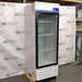 Straight-on studio view of a Fisher Isotemp GTFBG25RPGA upright laboratory refrigerator standing on a wooden pallet against a branded backdrop, featuring a full-length glass door, top-mounted digital controller, Fisherbrand logo, and lower ventilation louvers