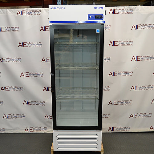 Straight-on studio view of a Fisher Isotemp GTFBG25RPGA upright laboratory refrigerator standing on a wooden pallet against a branded backdrop, featuring a full-length glass door, top-mounted digital controller, Fisherbrand logo, and lower ventilation louvers