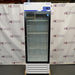 Straight-on studio view of a Fisher Isotemp GTFBG25RPGA upright laboratory refrigerator standing on a wooden pallet against a branded backdrop, featuring a full-length glass door, top-mounted digital controller, Fisherbrand logo, and lower ventilation louvers