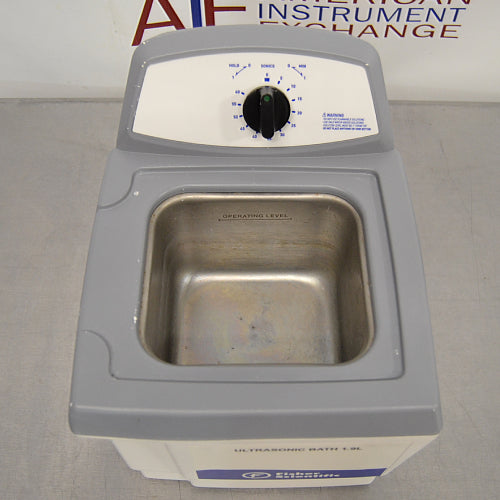 High-angle studio view of the Fisher Scientific M1800 1.9L ultrasonic bath with its lid removed, showing the open stainless steel interior tank with an "OPERATING LEVEL" fill line and the rear control panel with a mechanical timer knob