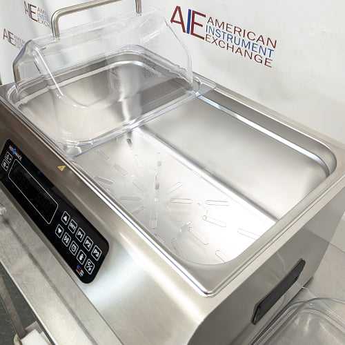 High-angled view of Four E's USA 24L Per4mance stainless steel water bath with one chamber open and empty, showing the bottom tray insert and digital control panel against an American Instrument Exchange background