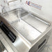 High-angled view of Four E's USA 24L Per4mance stainless steel water bath with one chamber open and empty, showing the bottom tray insert and digital control panel against an American Instrument Exchange background