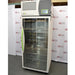 A front-facing view of the tall, upright Caron 7000-33-1 environmental chamber, highlighting its full-length glass door, distinctive bright green handle, and top-mounted control interface against an American Instrument Exchange backdrop.