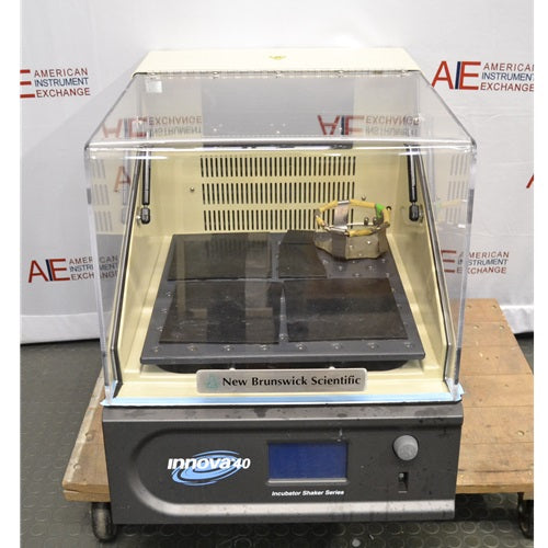 A front-facing view of the New Brunswick Innova 40R refrigerated incubator shaker, showing its clear acrylic lid, internal platform with a flask clamp, and the control panel labeled "Innova 40," positioned in front of an American Instrument Exchange backdrop.