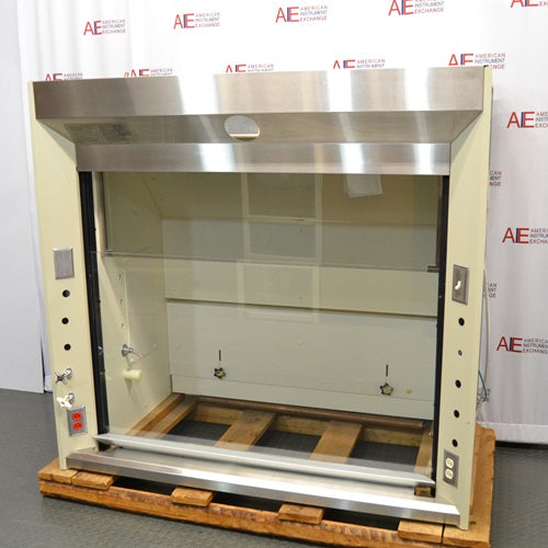 A front angle view of a Jamestown chemical fume hood mounted on a wooden pallet in front of an American Instrument Exchange backdrop, displaying its stainless steel upper header, clear glass sash, and side utility controls.