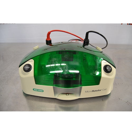 A front view of a Bio-Rad MicroRotofor Cell unit resting on a metallic surface, featuring a green tinted protective cover, connected red and black power leads, cooling and power rocker switches, and front branding labels.