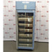 A front-facing view of a Helmer HPR-125 pharmacy refrigerator in front of an American Instrument Exchange backdrop, showing its glass door, internal stainless steel drawers, and top blue control panel.