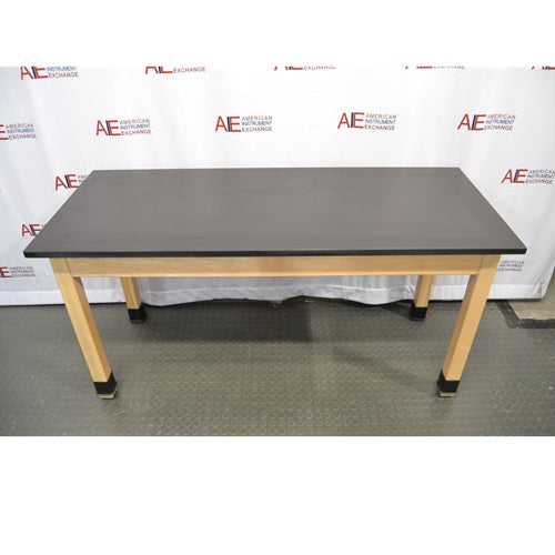 A straight-on front view of a wooden laboratory bench featuring a durable black epoxy resin work surface supported by light wood legs with protective black base caps against an American Instrument Exchange backdrop.