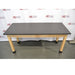 A straight-on front view of a wooden laboratory bench featuring a durable black epoxy resin work surface supported by light wood legs with protective black base caps against an American Instrument Exchange backdrop.