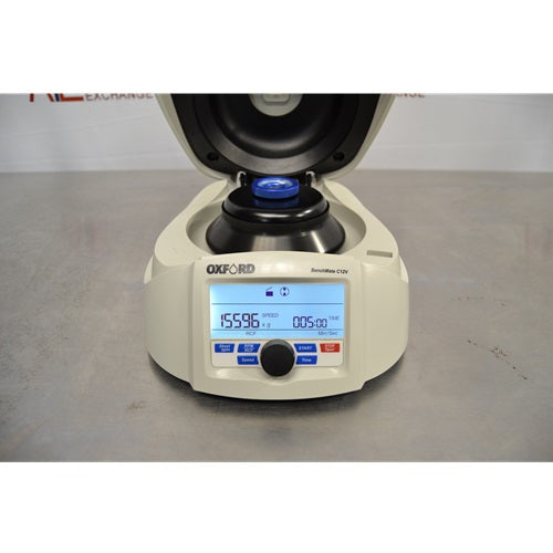 A front view of an open Oxford Lab Products Benchmate C12V microcentrifuge showing the internal rotor, central blue locking knob, control dial, and illuminated digital display screen with speed and timer settings against an American Instrument Exchange backdrop.