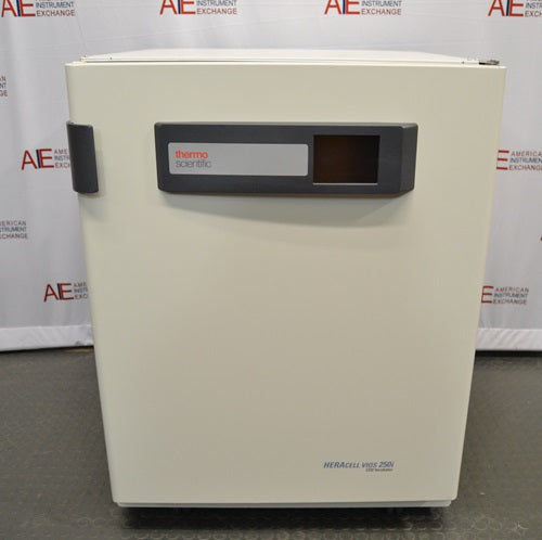 A front-facing view of a Thermo Heracell VIOS 250i LK CO2 incubator in front of an American Instrument Exchange backdrop, featuring a solid white outer door, a dark gray top control strip with touchscreen display, door latch, and Heracell VIOS 250i branding on the lower right.