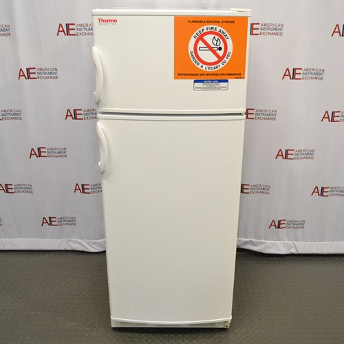 A full front view of a white Thermo Scientific 10FCEETSA flammable material combination refrigerator/freezer on a lab floor, showing the top freezer door with safety hazard warning sign and Thermo Scientific logo, lower refrigerator door, and side handles.