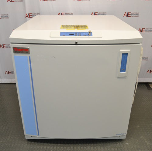 A front-facing view of a Thermo Scientific CryoPlus 4 cryogenic storage system sitting in front of an American Instrument Exchange backdrop, displaying its white exterior casing, blue accent stripe, Thermo Scientific logo, top microprocessor control panel with key lock, level indicator on the right, and bottom CryoPlus 4 branding.