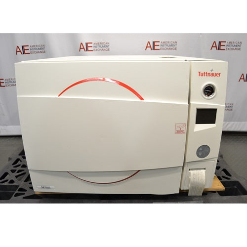 A front-facing view of a Tuttnauer 3870ELP-B/L-D benchtop autoclave sitting on a pallet, featuring a white main door with a red circular accents, Tuttnauer logo, digital display panel, pressure gauge, and built-in paper printer.