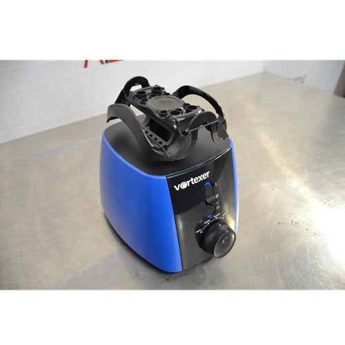 An elevated front-left view of a blue and black Heathrow Scientific Vortexer sitting on a stainless steel surface, showing the top tube holder attachment, front power switch, and speed dial control knob.