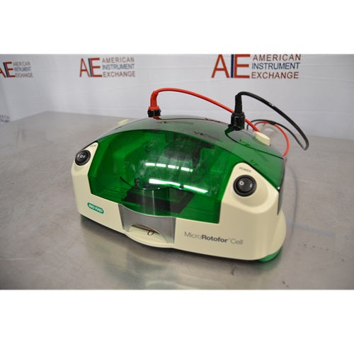 An elevated front-right view of a Bio-Rad MicroRotofor Cell unit set on a stainless steel tabletop, displaying the green protective cover, connected red and black power leads, power rocker switch, and American Instrument Exchange background banner.