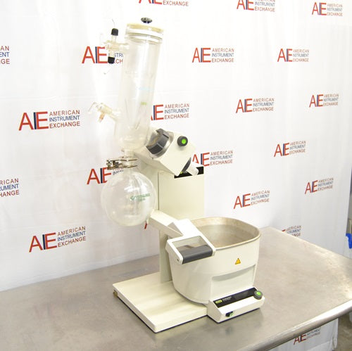 An elevated side view of a Buchi R-300 rotary evaporator system set on a stainless steel benchtop in front of an American Instrument Exchange backdrop, highlighting the glass condenser, receiving flask, motor drive unit, and heating bath.