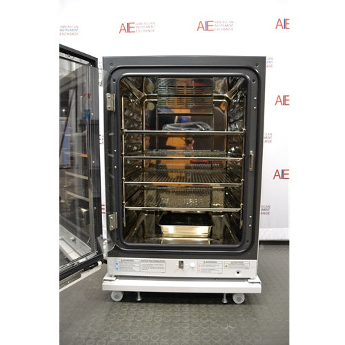 An interior view of an open-door PHCbi Cell-IQ series tri-gas cell culture incubator available from American Instrument Exchange, showing the internal shelving and stainless steel chamber.