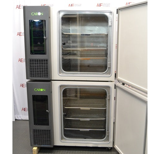 The interior view of a stacked Caron 6010-1 environmental chamber system with the outer doors open, revealing the stainless steel shelving inside each chamber, positioned in front of an American Instrument Exchange backdrop.