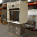 Three-quarter side-angled studio view of a Kewaunee 4-foot laboratory fume hood showing the beige upper enclosure, sliding glass sash, left side pillar with electrical outlets, and the stainless steel storage cabinet base
