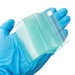 Close-up of a gloved hand holding a stack of clean glass microscope slides against a white background.