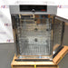 Front-angled view of an open Memmert HPP260 climate chamber resting on a wooden shipping pallet, displaying the polished stainless steel interior chamber fitted with wire shelving racks, rear ventilation ports, and the top digital control panel.