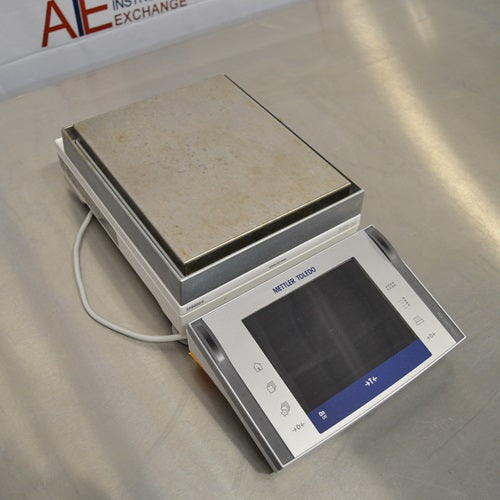 Angled view of a Mettler Toledo XPE6002S precision balance showing the stainless steel weighing pan and front touchscreen terminal.