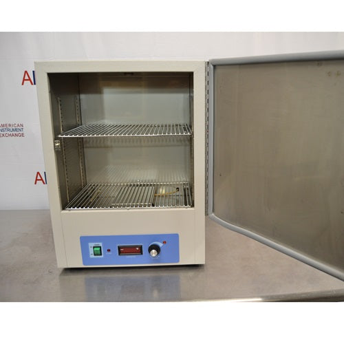 An open front view of a Thermo Scientific PR305225M Precision mechanical convection oven resting on a stainless steel surface in front of an American Instrument Exchange backdrop, with its front door swung open to reveal the interior chamber housing two wire rack shelves and the bottom blue control panel.